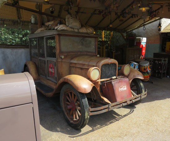 A brown, old-timey car that looks likes it's been used to ferry medicine between remote villages. It's parked inside an open-air gift shop with wooden balls hanging from the ceiling.