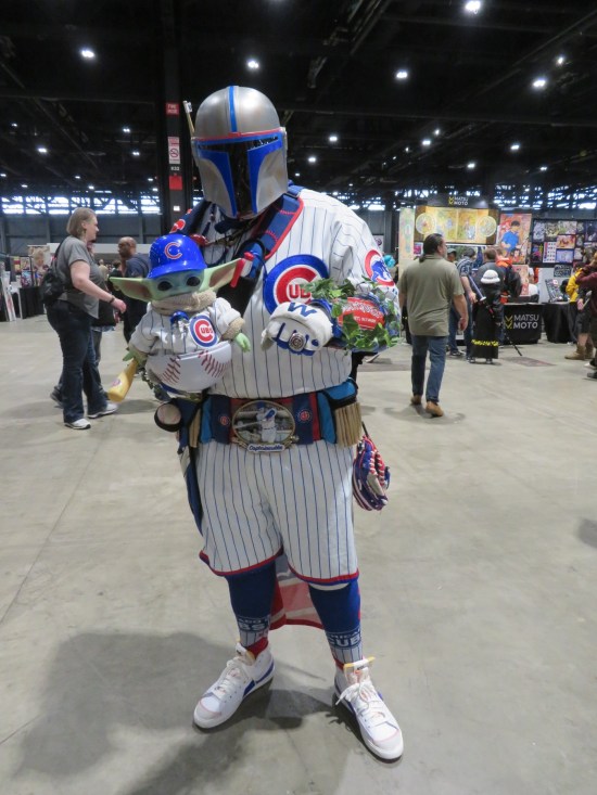 Mandalorian cosplayer holding a stuffed Baby Yoda, both wearing Chicago Cubs uniforms.