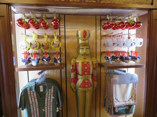 Christmas items for sale include red ball ornaments, Mickey Mouse ear ornaments, green polo shirts, and rugs. A five-foot-tall faux-brass Nutcracker stands amid the racks.