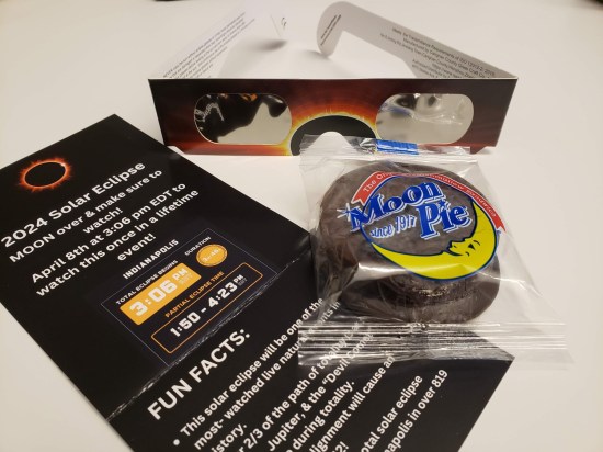 A pair of eclipse glasses, a brochure with 2024 eclipse data and trivia, and a Moon Pie.