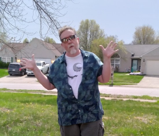 Me doing jazz hands while wearing eclipse glasses, Moon Knight T-shirt, and green Hawaiian shirt that looks oddly blue.
