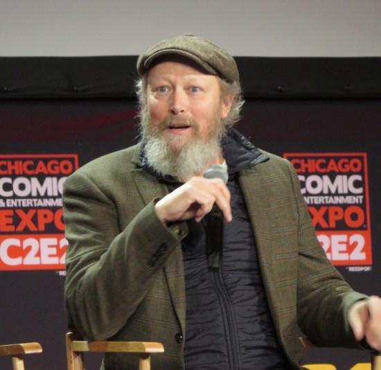 Lars Mikkelsen sitting agape onstage with mic.