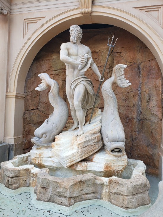 White stone sculpture of the god Neptune flanked by two large, angry fish standing on their chins.
