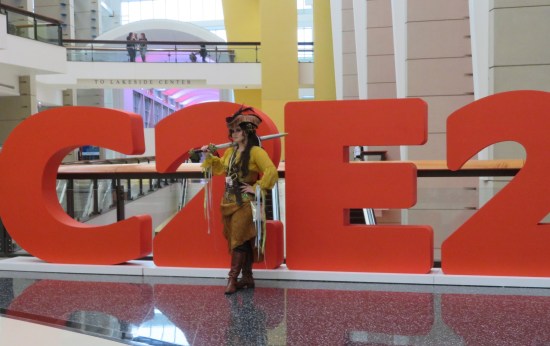 Pirate woman stands in front of giant red C2E2 letters in the convention center lobby.