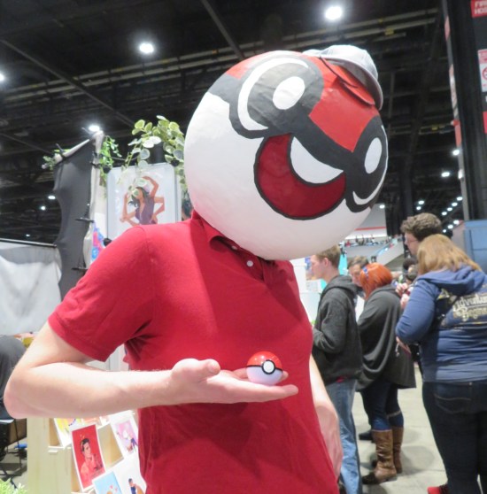 Man wearing a Pokeball for a helmet, holding a toy Pokeball up in one hand.