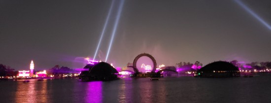 Pulled back for wider lagoon shot. Gateways are purple, spotlights shooting like lasers into the sky, much light pollution renders the night sky light grey
