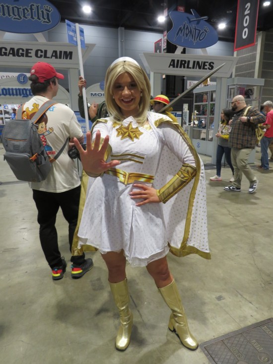 Cosplayer as Starlight, white with gold trim, posing in front of the massive Funko area.
