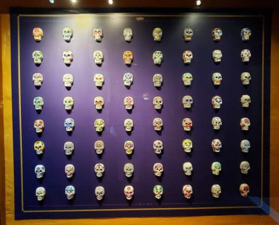 64 tiny skulls painted differently and hung in eight even rows inside a display case with a purple backing.