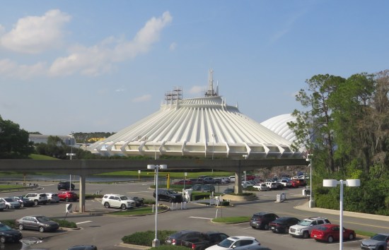 Large white circular building with ridged, angled roof that tapers upward into a smaller, still-circular roof. Full parking lot out front.