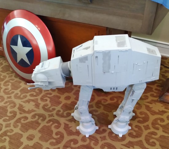 A Star Wars AT-AT toy/playset and a Captain America shield, both positioned on an ugly carpet.