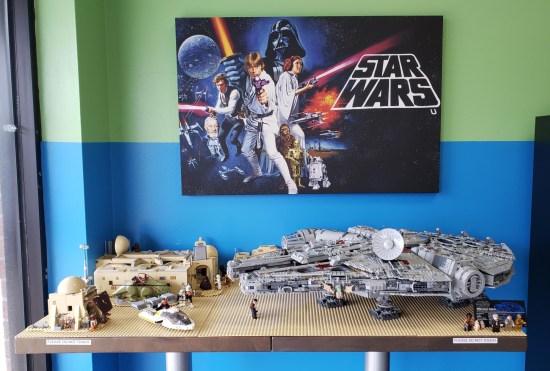 Lego Millennium Falcon and Lego Cantina on a table under a Star Wars poster.