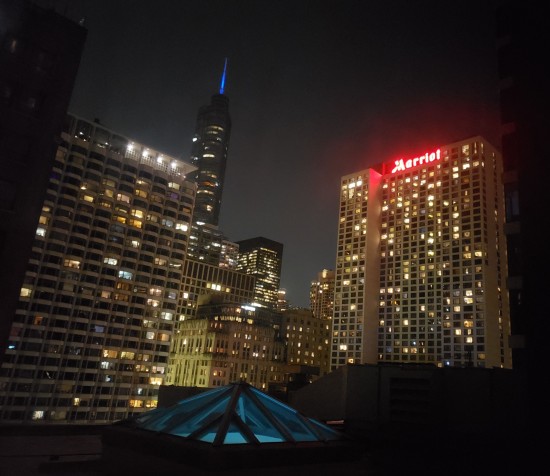 Nighttime view of a cross-section of Chicago's Magnificent Mile. Lit-up things include many windows, a Marriott logo with the second T obscured by a building corner, and the lightsaber atop Trump Tower.