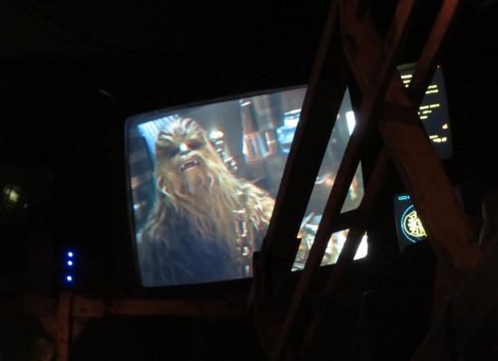 Wall-mounted TV with Chewbacca yelling. Catwalk rails obscure the right side.