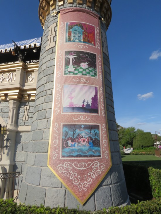 Large vertical banner hangs from tall castle tower with four pieces of Cinderella movie design art.