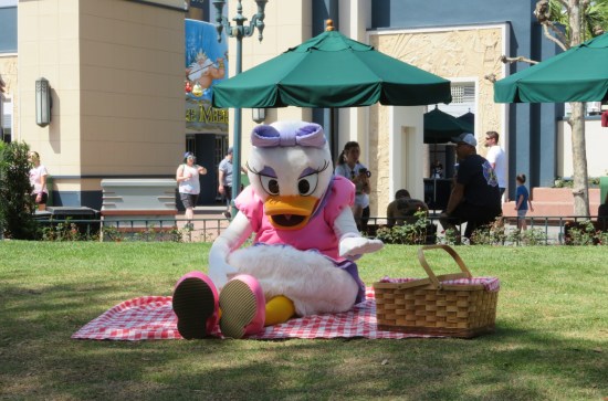 Cast member in Daisy Duck costume sitting on a picnic blanket with basket at hand.