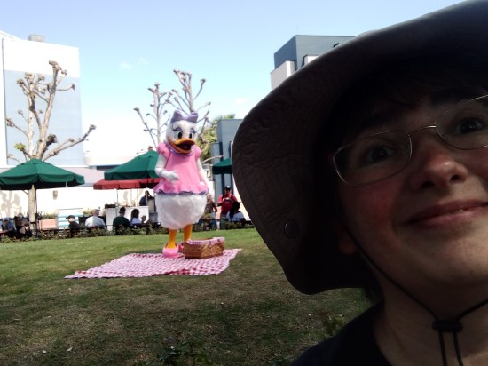 Anne taking a heavily shadowy selfie with Daisy Duck in the distance, small enough to resemble a tiny sprite that's shouting in her ear.