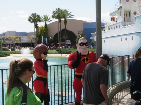 Disney World cast members playing Elastigirl and Mr. Incredible by a fenced pond. Palm trees in the background.