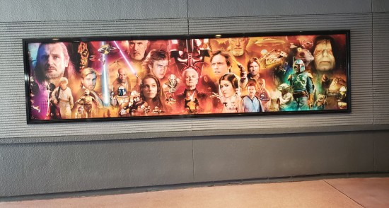 20-foot-wide poster with characters from the first six Star Wars films in random order. Background colors are graded from pink to orange to yellow. It hangs on a bleak wall with decaying baseboards.