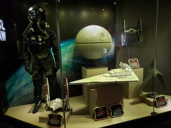 Display case with TIE Fighter Pilot costume and miniatures of the Death Star, a TIE Fighter, a Star Destroyer, an Imperial Shuttle, and a Y45 AT-Hauler.