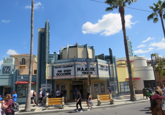 Majestic Theater marquee promising "glitz & glamour for every occasion...where the stars shine.| Sidewalk has yellow benches and palms.
