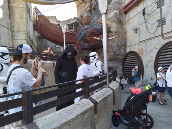 Kylo Ren cosplayer interrogates a Rey cosplayer while a sequel Stormtrooper watches, as do tourists with phones out.