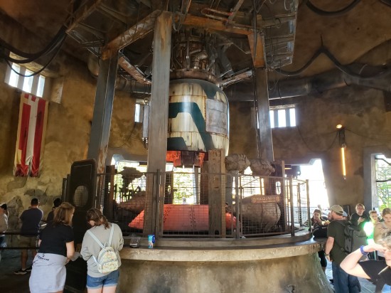 Giant fake cylindrical machinery with stand-up restaurant table around its perimeter.