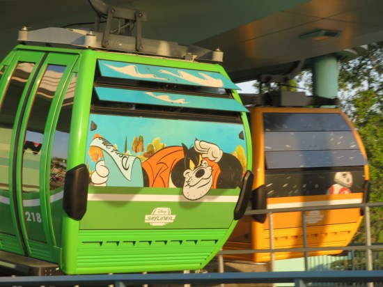 Cable car near the ground with an ornery Black Pete in its cartoon window, sidling next to a cable car with BB-8 in its window.