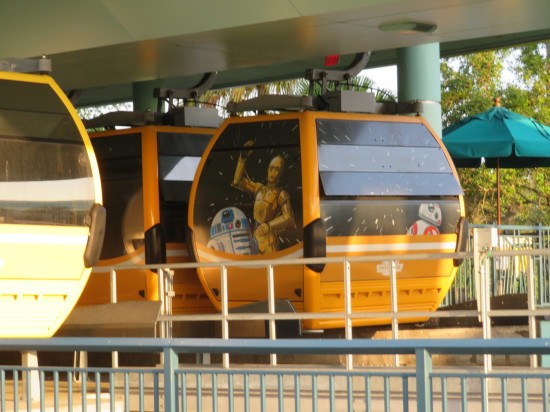 Yellow cable car reaching ground level. Windows are painted with C-3PO, R2-D2 and BB-8 against a hyperspace backdrop.