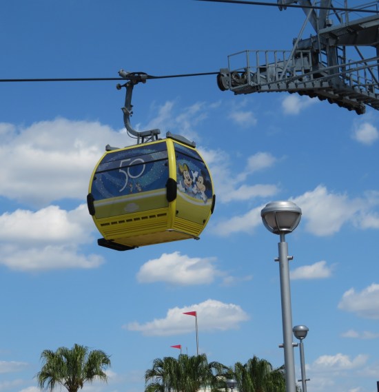 Cable car with Mickey and Minnie Mouse drawn on its cartoon windows. It's high above, with palm trees well below.