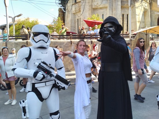 Stormtrooper, Rey and Kylo Ren cosplayers pose for cameras. The two Force users have arms outstretched in power gestures. Lots of staring tourists.