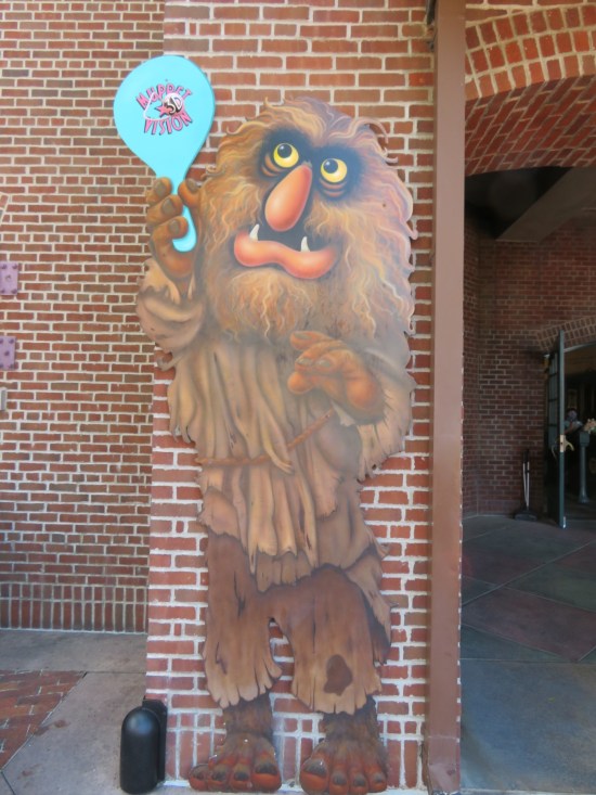 Cardboard standee of the giant Muppet Sweetums against a brick doorway. He's holding a Muppet Vision 3-D ping-pong paddle.