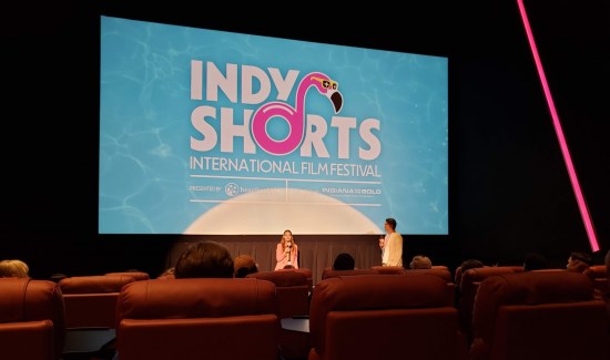 Fourth-row vantage of the filmmaker and our host chatting at the front of the theater. The INDY SHORTS logo is large onscreen behind them.