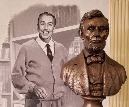 Bronze Lincoln bust on a pedestal in front of a black-and-white painting of Walt Disney.