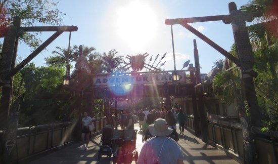 Wood bridge with Adventureland sign overhead.  Camera is pointed into the sun. Anne is walking ahead of me.