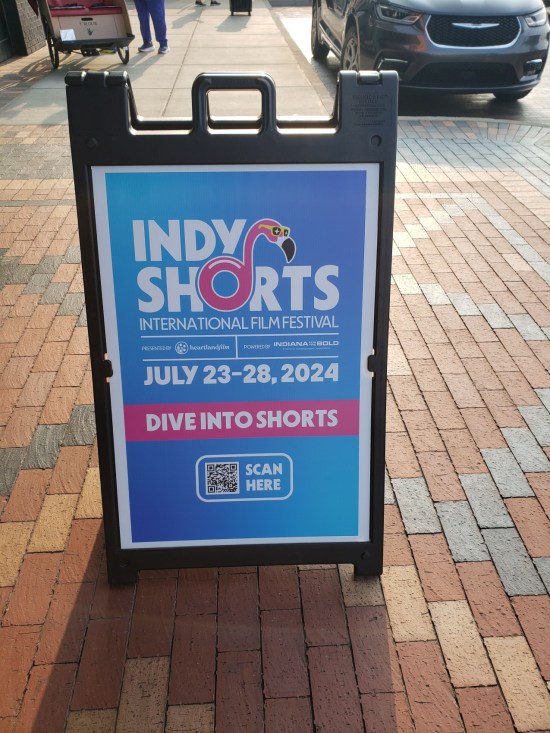 Sandwich board touting the Indy Shorts Film Festival on a brick sidewalk.