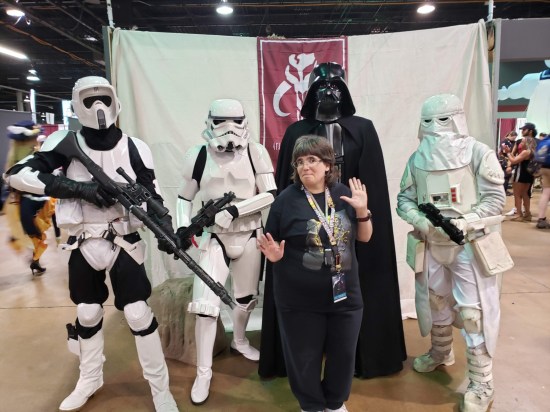 Anne kindasorta putting her hands up while surrounded by cosplayers: Stormtrooper, Snowtrooper, Biker Scout and Darth Vader.