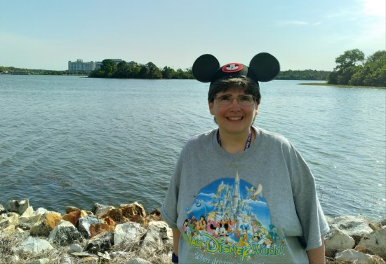 Anne standing by the lagoon, wearing her new Mickey ears and Disney World T-shirt.