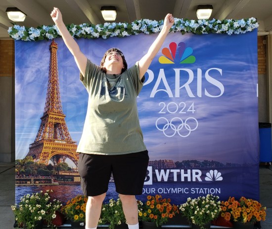 Anne standing on the same fake Olympic platform as in our lead photo, eyes closed and arms triumphantly skyward.