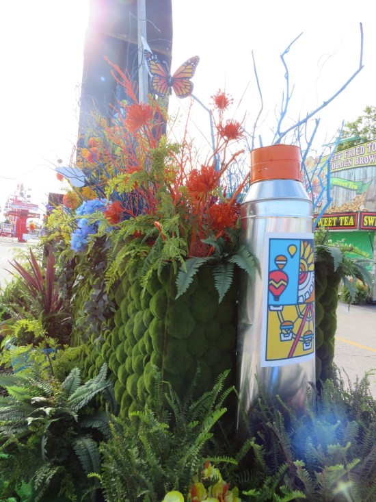 Behind the arch base, large paint tube and flowers with a fake butterfly on top.