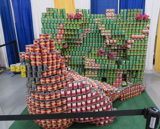 Cardinal made of cans in front of a wall of cans with real peonies on it.
