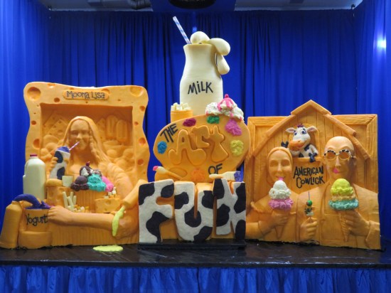 cheese sculpture of the Mona Lisa drinking milk from a cow-patterned bottle with a straw, the "American Gothic" farmer couple eating ice cream cones and wearing sunglasses, and the logo "THE ART OF FUN" between them with a sculpted quart bottle of milk on top.