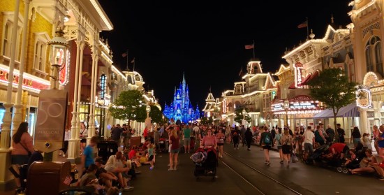 Faraway view of Cinderella Castle at night. Brightly lit shops flank either side of the path to it. People are EVERYWHERE.