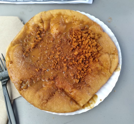 An elephant ear that takes up an entire 12-inch paper plate, topped with cookie crumbles and sweet brown liquid.