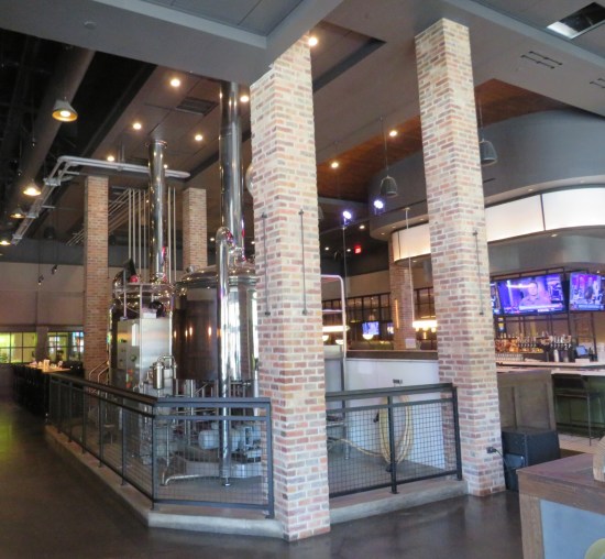 Large brewing still in the middle of a restaurant with tall ceilings and industrial-chic decor.