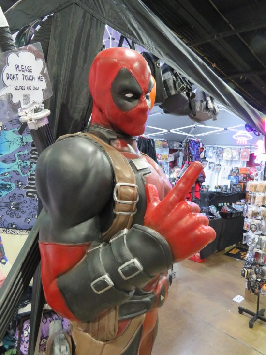 A Deadpool statue next to an exhibitor booth, loosely resembling the Ed McGuinness version.