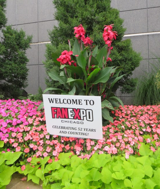 Bright flower bed with roses and greenery. In the middle is a sign: "Welcome to Fan Expo Chicago, celebrating 52 years and counting!"