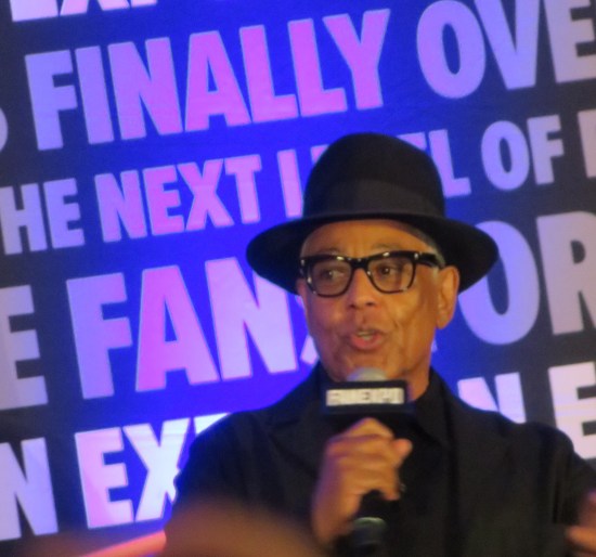 Giancarlo Esposito talking onstage against a purple backdrop of Fan Expo pamphlet verbiage.