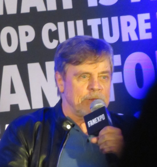 Closeup of Hamill still talking into a mic onstage.