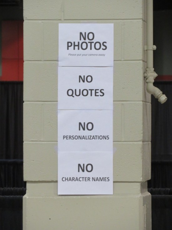 Four sheets of paper taped to a column in the middle of an exhibit hall reading, "No photos, please put your camera way. No quotes. No personalizations. No character names."