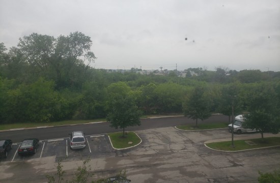Smudged window view of an empty hotel parking lot and lots of urban forest beyond.